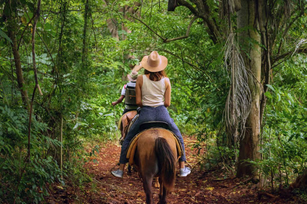 Woman riding horse through tropical forest